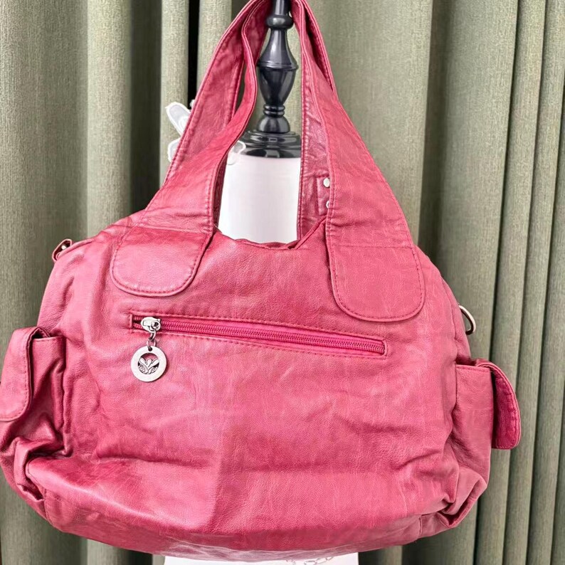 May include: A large, red handbag with a zippered pocket and two side pockets. The bag has a silver charm on the zipper and a shoulder strap. The bag is made of a soft, textured material.