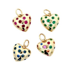 May include: Four gold heart-shaped pendants with colorful gemstone accents. Each pendant features a different arrangement of gemstones, including red, green, blue, and a mix of colors. The pendants have a polished finish and a loop for attaching to a chain.