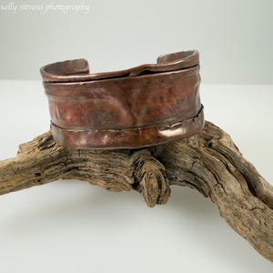 May include: A wide copper bracelet with a hammered finish. The bracelet is made of thick copper and has a rustic, organic look.