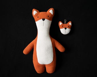 May include: Two plush fox toys, one large and one small. The larger fox is orange with a white belly and black eyes. The smaller fox is a keychain with a similar design.