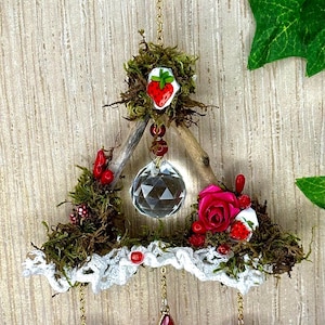 Peut inclure: Suspension murale artisanale et fantaisiste. Elle présente un cadre triangulaire en bois orné de mousse, d'une boule de cristal transparente, et d'une rose rose. Comprend des accents rouges, un charme de fraise et des pendentifs rouges.