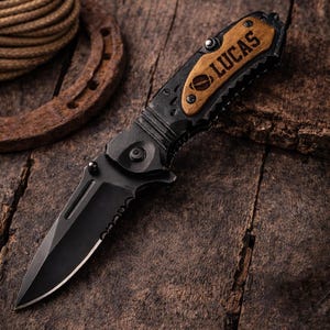 May include: A black folding knife with a serrated edge and a wooden handle engraved with the name "LUCAS". The knife is set against a rustic wooden background, with a horseshoe and rope in the background.