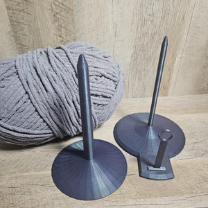 May include: Two black 3D printed yarn holders with a gray yarn ball. The yarn holders have a round base and a tall, thin spike.