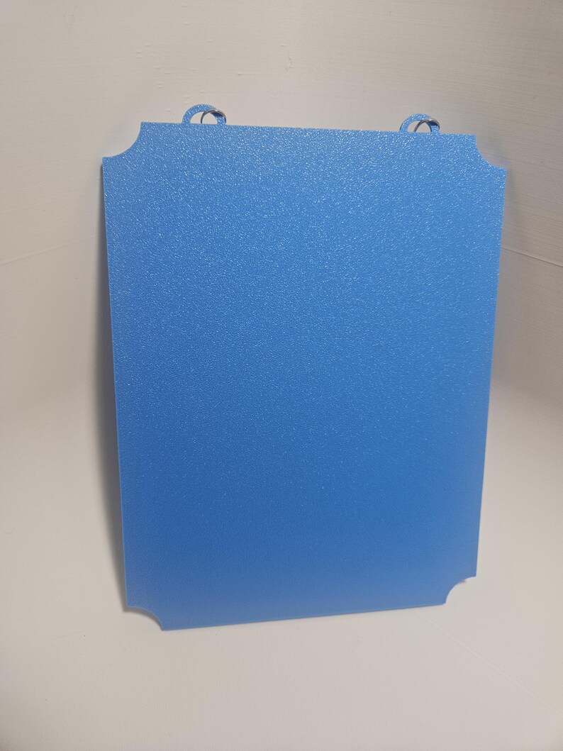 May include: A rectangular, light blue sign with rounded corners and two small, looped handles at the top. The sign has a textured surface and a solid blue color.