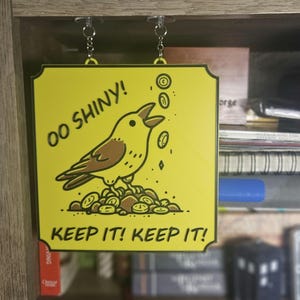 Può includere: Un cartello giallo con un uccello dei cartoni animati e il testo "OO SHINY! KEEP IT! KEEP IT!" L'uccello è marrone e giallo e tiene un mucchio di monete d'oro.