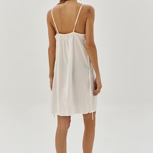 May include: A white slip dress with thin straps and a gathered neckline. The dress is made of a lightweight fabric and has a relaxed fit.