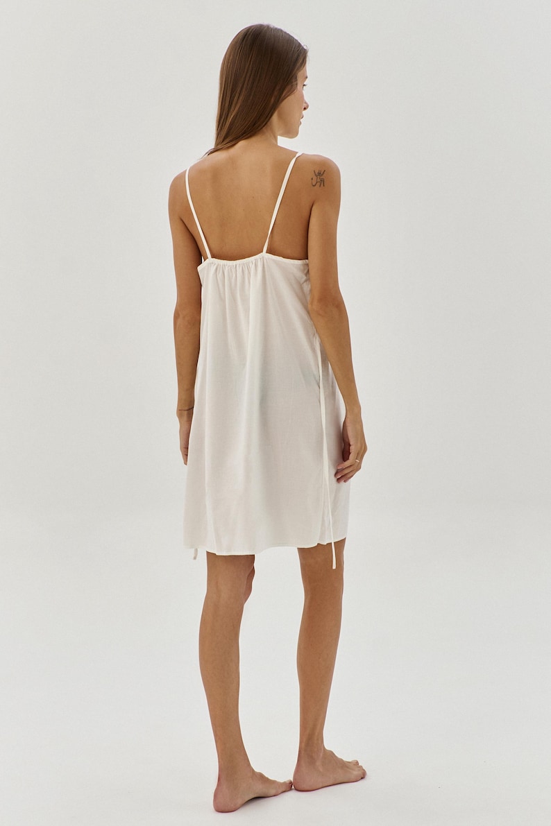 May include: A white slip dress with thin straps and a gathered neckline. The dress is made of a lightweight fabric and has a relaxed fit.