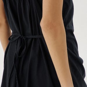 May include: A black sleeveless dress with a tie at the waist. The dress has a gathered neckline and a flowing skirt.