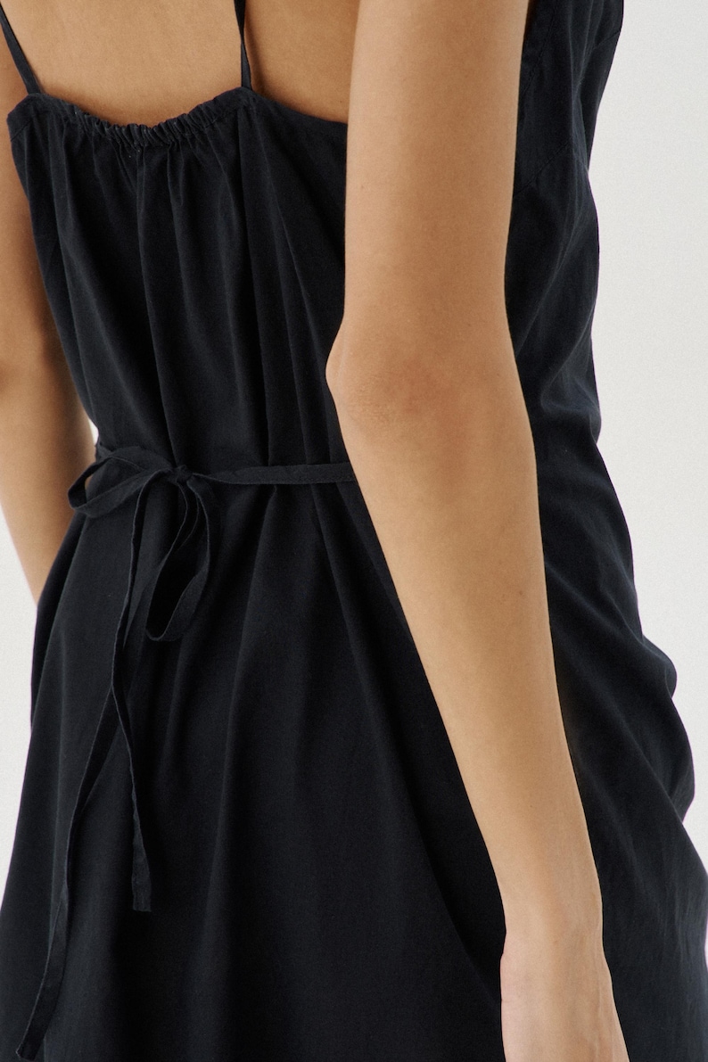 May include: A black sleeveless dress with a tie at the waist. The dress has a gathered neckline and a flowing skirt.