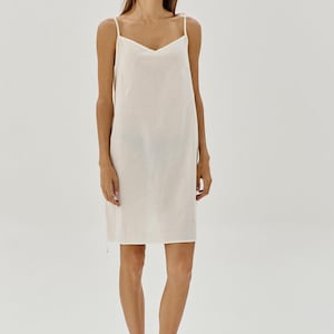 May include: A white sleeveless slip dress with a V-neckline. The dress is made from a soft, lightweight fabric and has a relaxed fit.