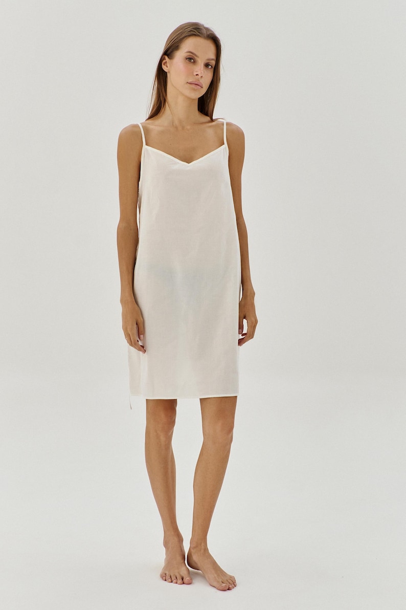 May include: A white sleeveless slip dress with a V-neckline. The dress is made from a soft, lightweight fabric and has a relaxed fit.