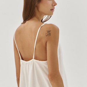 May include: A white sleeveless top with a scoop neck and a loose fit. The top is made from a soft, lightweight fabric and has a relaxed, casual style.