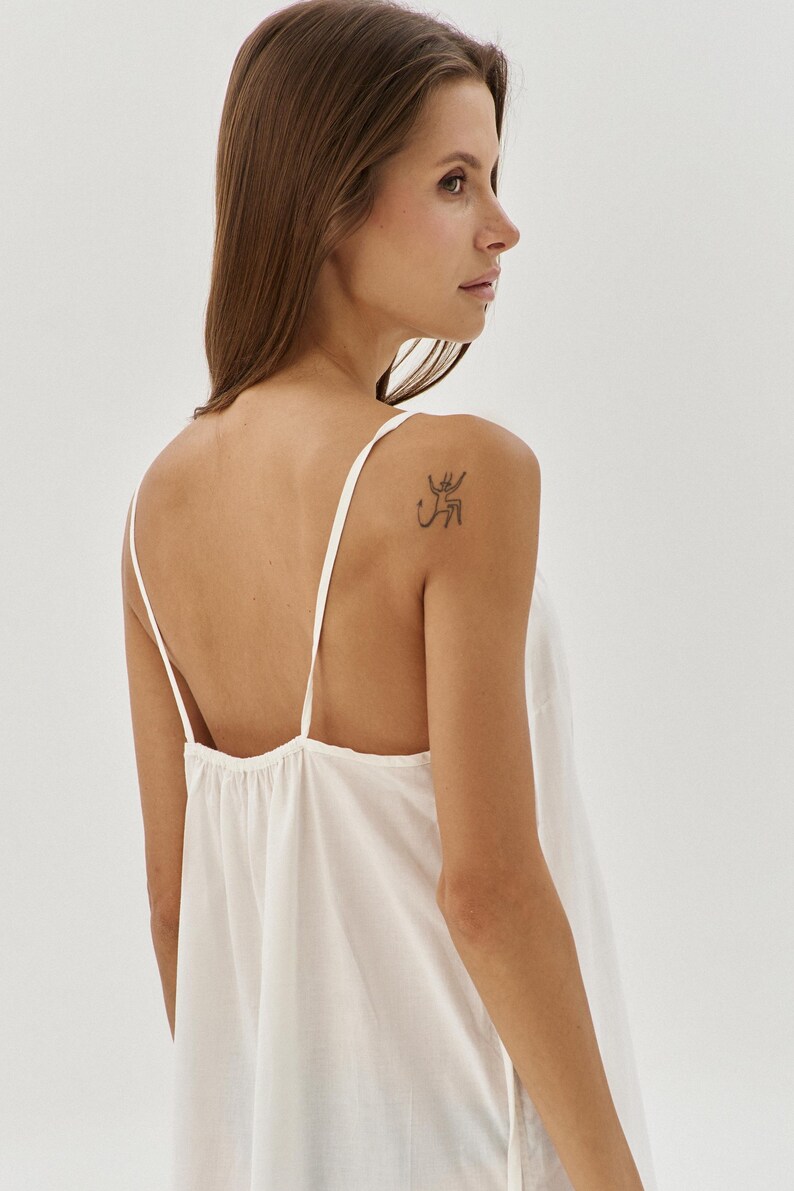 May include: A white sleeveless top with a scoop neck and a loose fit. The top is made from a soft, lightweight fabric and has a relaxed, casual style.
