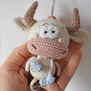 May include: A crocheted white and brown bull with pink nose and blue ice skates. The bull has black eyes and a white face.