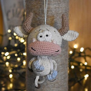 May include: A white crocheted bull ornament with pink nose and blue ice skates hanging from a silver string.