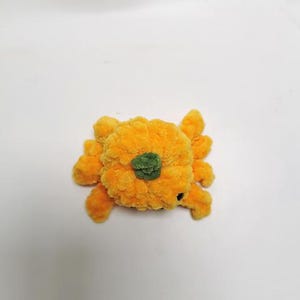 以下が含まれることがあります： 緑色の茎が付いたオレンジ色の毛糸で編まれたかぼちゃ。かぼちゃは手作りの玩具です。