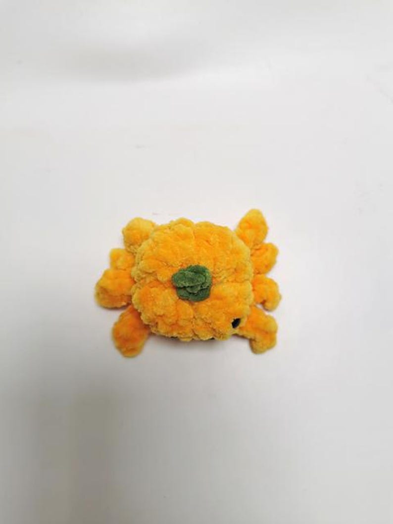 以下が含まれることがあります： 緑色の茎が付いたオレンジ色の毛糸で編まれたかぼちゃ。かぼちゃは手作りの玩具です。