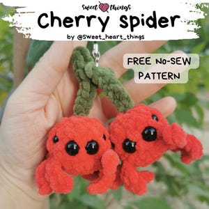 May include: Two red crocheted cherry spiders with black eyes and green stems. The spiders are attached to a keychain. The image includes the text "Cherry Spider" and "FREE No-Sew PATTERN".