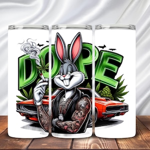 May include: A white tumbler with a cartoon Bugs Bunny design. The character has tattoos and is smoking a cannabis cigarette. The word "DOPE" is in green block letters. A red car and cannabis leaves are also in the design.
