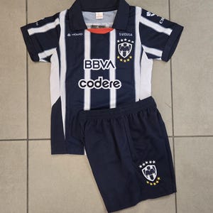 May include: A blue and white striped football shirt with the text "BBVA codere" and a team logo. The shirt is paired with matching blue football shorts with a team logo.