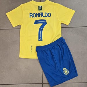May include: A yellow soccer jersey with blue trim and the name "RONALDO" and the number "7" on the back. The jersey is paired with blue soccer shorts with a team logo.