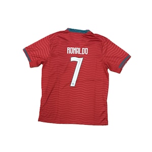 May include: A red short-sleeved sports jersey featuring a subtle wavy line pattern throughout. The back displays the name RONALDO in white capital letters above the number 7, which is also in white with a small emblem at the base. The collar and sleeve cuffs are trimmed in dark green.