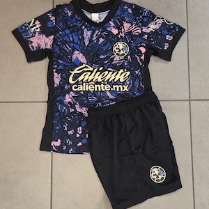 May include: A black and blue soccer jersey with a floral pattern and the text "Caliente caliente.mx". The jersey is paired with black soccer shorts featuring a team logo.