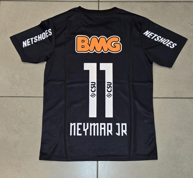 Pu&ograve; includere: Maglia nera con il numero 11 in bianco, il nome "NEYMAR JR" in bianco e il logo "CSU". La maglia presenta anche il logo "BMG" in arancione e bianco e il logo "NETSHOES" in bianco sulle maniche.