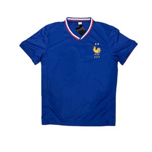 May include: A royal blue short-sleeved jersey with a V-neck collar featuring red and white trim. The chest displays an embroidered yellow rooster emblem above the letters FFF and two small yellow stars positioned above the rooster icon.