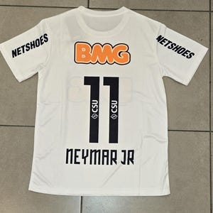 Pu&ograve; includere: Maglia sportiva bianca con il numero 11 nero, il nome "NEYMAR JR" e i loghi "NETSHOES" e "BMG". La maglia presenta anche il logo "CSU".