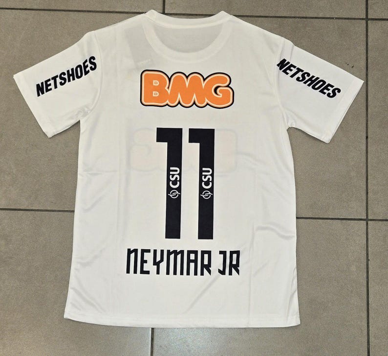 Pu&ograve; includere: Maglia sportiva bianca con il numero 11 nero, il nome "NEYMAR JR" e i loghi "NETSHOES" e "BMG". La maglia presenta anche il logo "CSU".