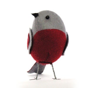 May include: A grey and red felt bird with a black beak and black eyes. The bird has wire legs and a long tail.
