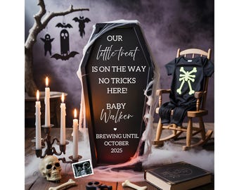 May include: A black coffin-shaped sign with white text reading "OUR little treat IS ON THE WAY NO TRICKS HERE! BABY Walker BREWING UNTIL OCTOBER 2025" draped in faux spiderwebs, accompanied by a black baby onesie with a yellow skeleton print.