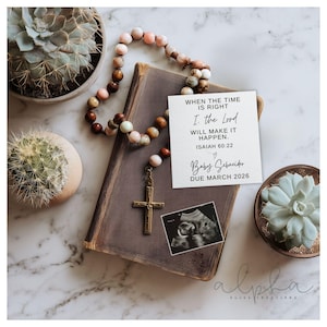 Puede incluir: Una tarjeta de anuncio de embarazo con el texto "WHEN THE TIME IS RIGHT I, the Lord WILL MAKE IT HAPPEN. ISAIAH 60:22" y "Baby Schneider DUE MARCH 2026". La tarjeta descansa sobre un libro marrón con un rosario y una cruz dorada.