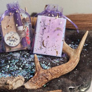 Puede incluir: Dos pequeñas bolsas moradas con purpurina dorada y estrellas, que contienen una botella morada, un pequeño frasco y una tarjeta que dice "Spiritual Aura Spell". Las bolsas están sobre una superficie peluda marrón con cuernos.