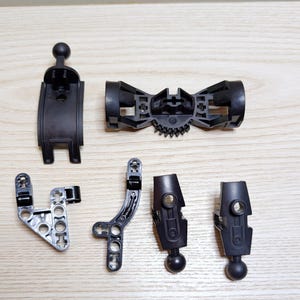 Op de afbeelding: Assortiment van zwarte plastic bouwsteentjes, waaronder gebogen stukken, connectoren en kogelgewrichten. De onderdelen zijn gerangschikt op een licht houten oppervlak, waarbij hun verschillende vormen en verbindingspunten worden getoond.