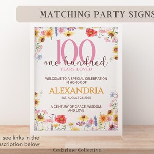 May include: A framed party sign with floral accents. The sign reads "100 Years Loved" with the name "Alexandria" and the date "August 23, 2025". The sign is decorated with a floral border and the text "Matching Party Signs".