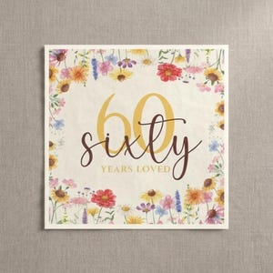May include: A square card with a floral border featuring yellow, red, and purple flowers. The card displays the number "60" in gold script, with the word "sixty" below it, and "years loved" underneath.