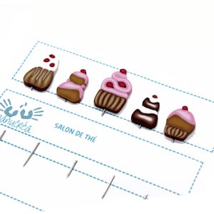 Könnte beinhalten: Fünf bunte Cupcake-förmige Pins auf weißem Hintergrund mit dem Text "Salon de The".