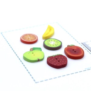 Può includere: Un assortimento di bottoni a forma di frutta: banana, fetta d'arancia, fetta di kiwi, mela, fragola e una mela rossa. Questi bottoni colorati, realizzati in materiale liscio, sono perfetti per cucito o lavori manuali.