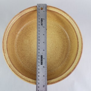 May include: A large, round, yellow ceramic bowl with a textured, rippled surface. The bowl is approximately 9 inches in diameter.