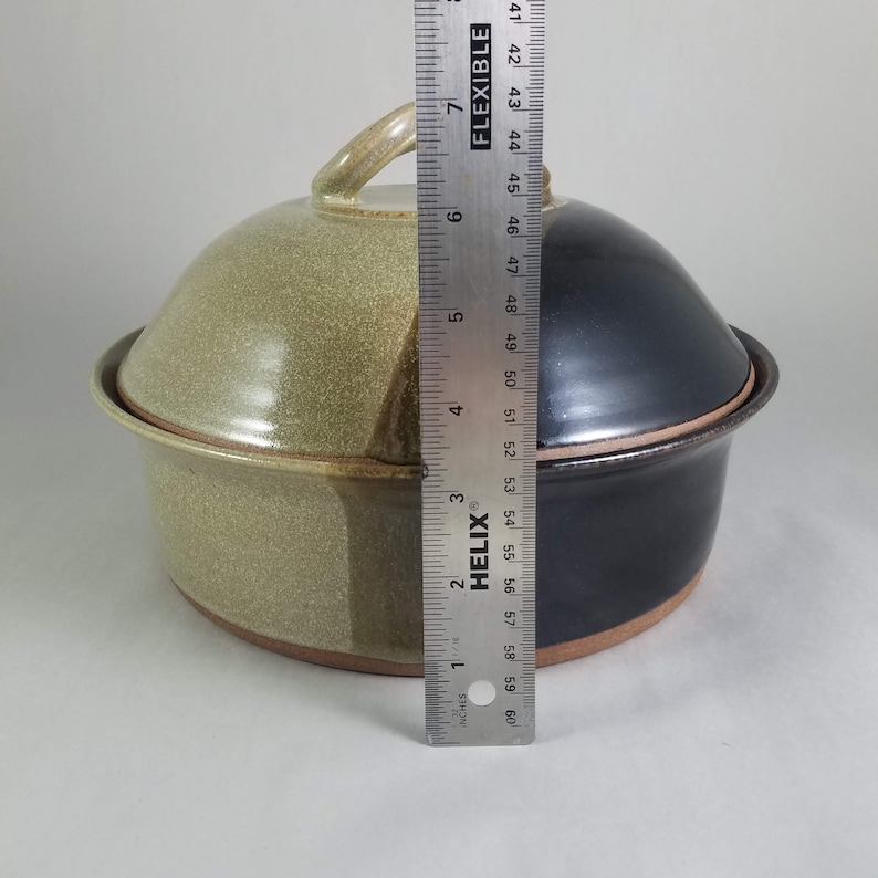 Pu&ograve; includere: Una pirofila in ceramica bicolore con coperchio. Il lato sinistro &egrave; beige e il destro &egrave; nero. Il coperchio ha una maniglia. Un righello mostra che il piatto &egrave; alto circa 15 cm.