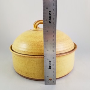 May include: A yellow ceramic casserole dish with a lid. The dish has a brown rim and a brown handle on the lid. The dish is 6 inches in diameter.
