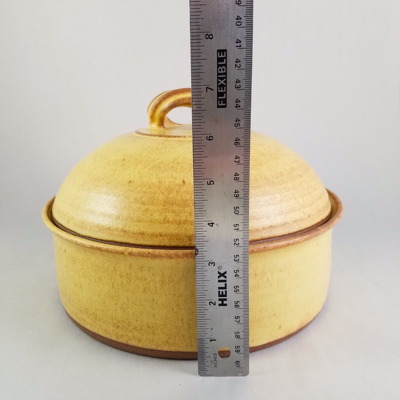 May include: A yellow ceramic casserole dish with a lid. The dish has a brown rim and a brown handle on the lid. The dish is 6 inches in diameter.