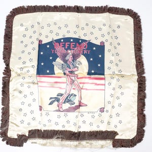 May include: Cream-colored decorative pillow with a brown fringe border. The pillow features a patriotic design with an illustration of a figure in red and white stripes, a blue background with white stars, and the text "DEFEND YOUR COUNTRY".