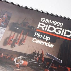 Peut inclure: Calendrier Ridgid Pin-Up de 1989-1990, avec une couverture noire et du texte blanc, ainsi qu'une bande rouge. Le calendrier pr&eacute;sente des images d'outils et une pin-up. Il est reli&eacute; en spirale.