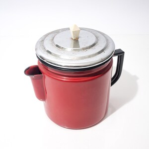 May include: A vintage red enamel coffee pot with a silver lid and black handle. The pot has a small spout on the side and a cream-colored knob on the lid. A classic kitchenware item.
