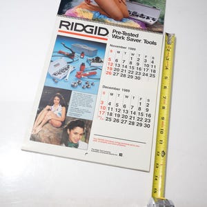 Peut inclure: Un calendrier RIDGID vintage de 1989, avec des images d'outils et de femmes. Le calendrier est ouvert sur novembre et d&eacute;cembre, avec un m&egrave;tre ruban jaune &agrave; c&ocirc;t&eacute;. Le calendrier mesure environ 25 cm de long.