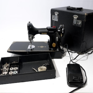 Pode incluir: Uma máquina de costura Singer preta vintage com detalhes dourados, incluindo uma mala de transporte preta, um pedal preto e uma caixa de acessórios preta contendo bobinas de metal e vários calcadores.