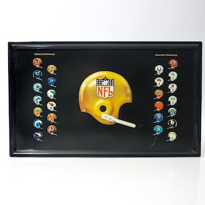 Peut inclure: Plateau rectangulaire noir avec un casque de football américain jaune au centre, orné du logo NFL. Le plateau présente des casques d'équipes des deux côtés, représentant les conférences nationale et américaine.